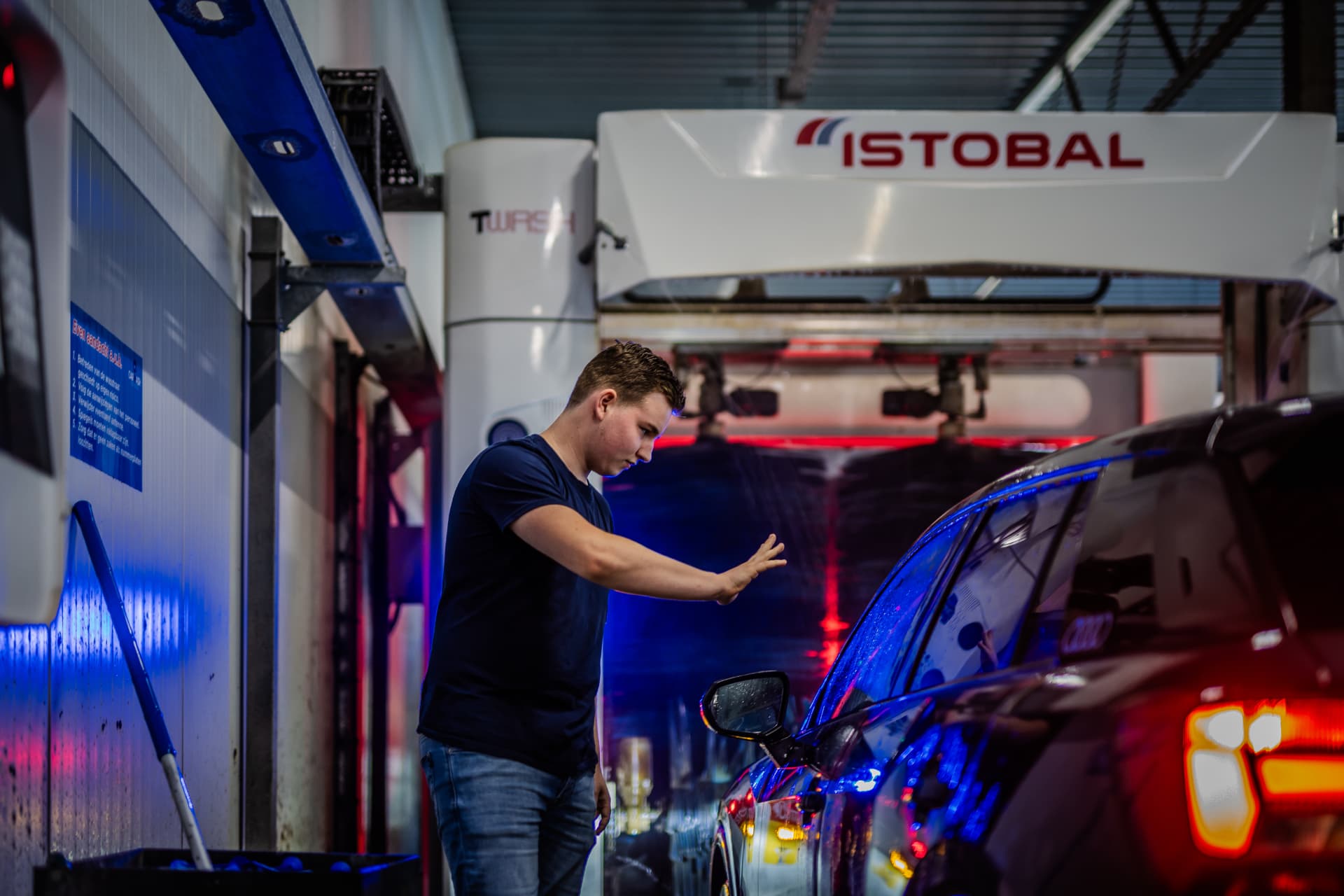 Medewerker begeleidt een auto de wasstraat in