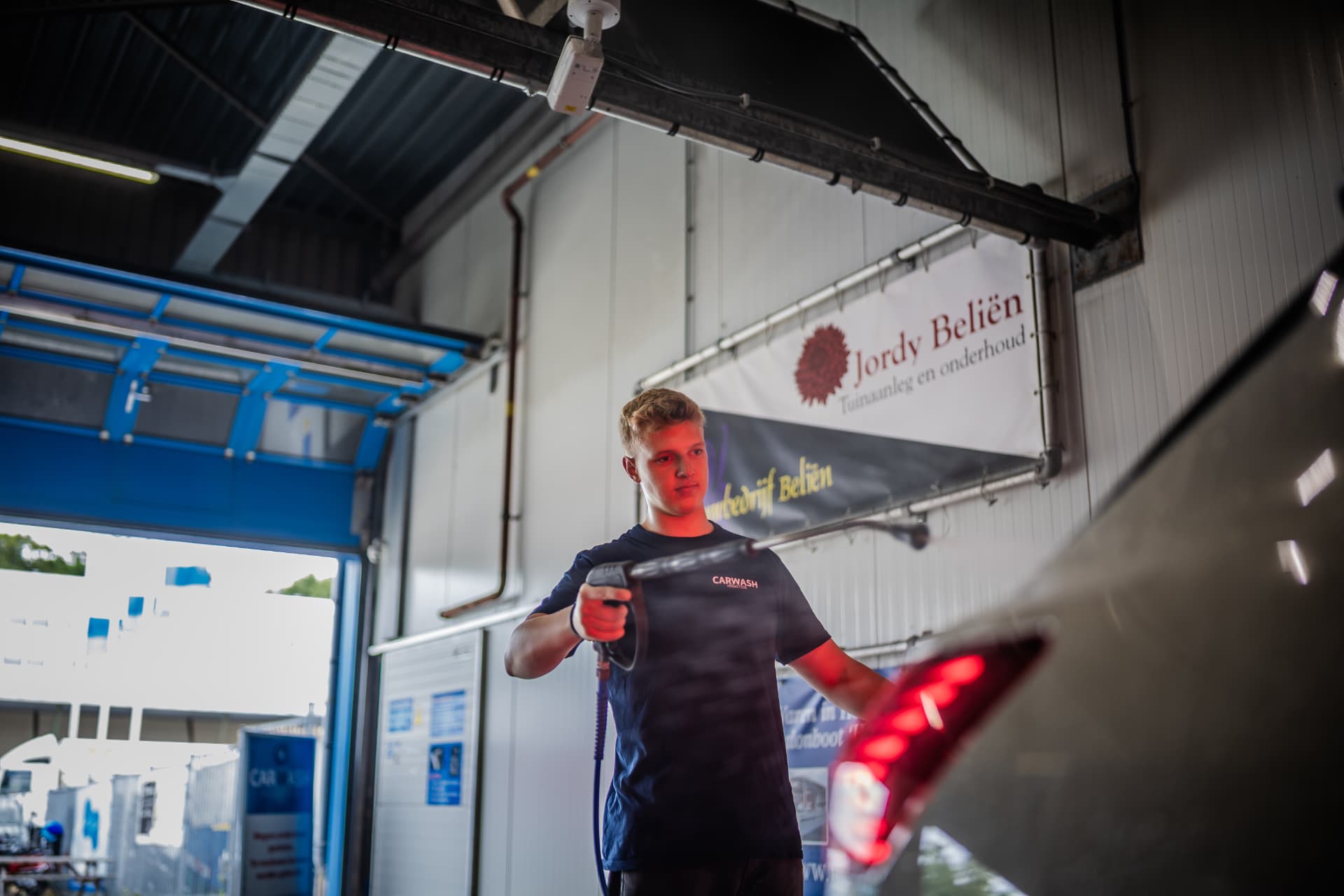 Medewerker spuit een auto af in de wasbox